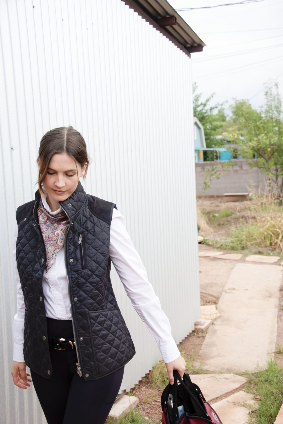 A rider in a black Chestnut Bay Heritage quilted vest carrying a bag outside the barn