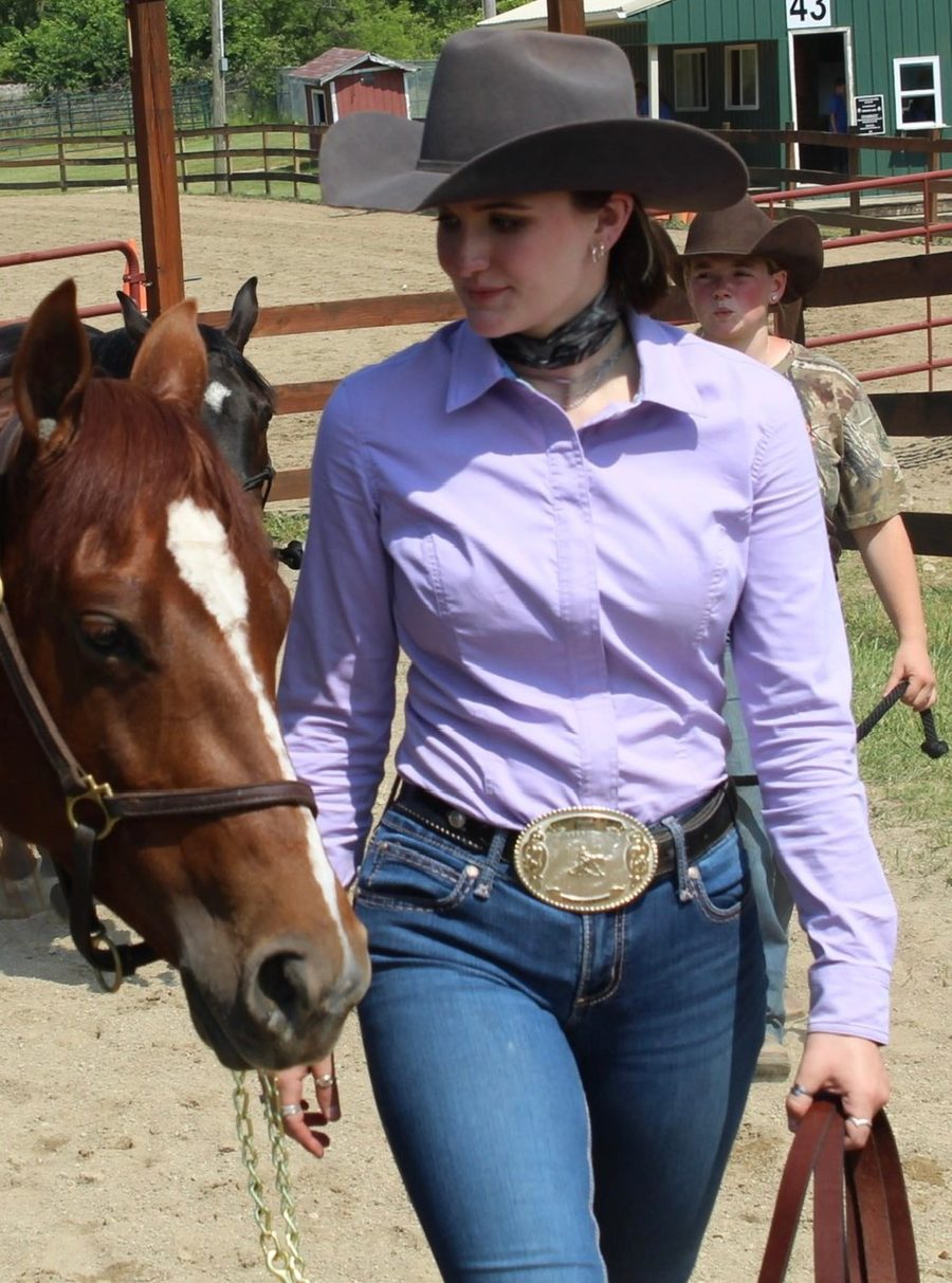 A western rider in a lavender Chestnut Bay Annie-O show shirt and cowboy hat leading her chestnut horse