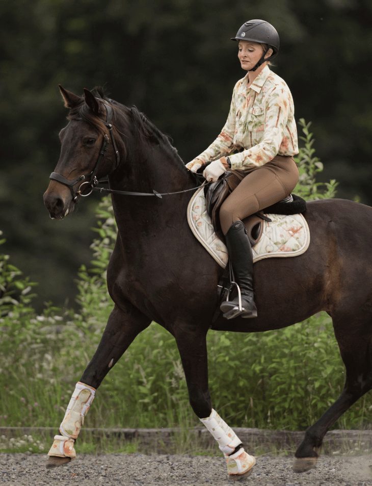 A rider in a Dapplebay Vintage Floral top on her dark bay horse in a matching saddle pad and boots