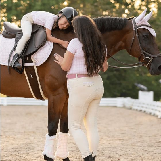 A young rider in a Dapplebay top leaning down from her horse to a friend
