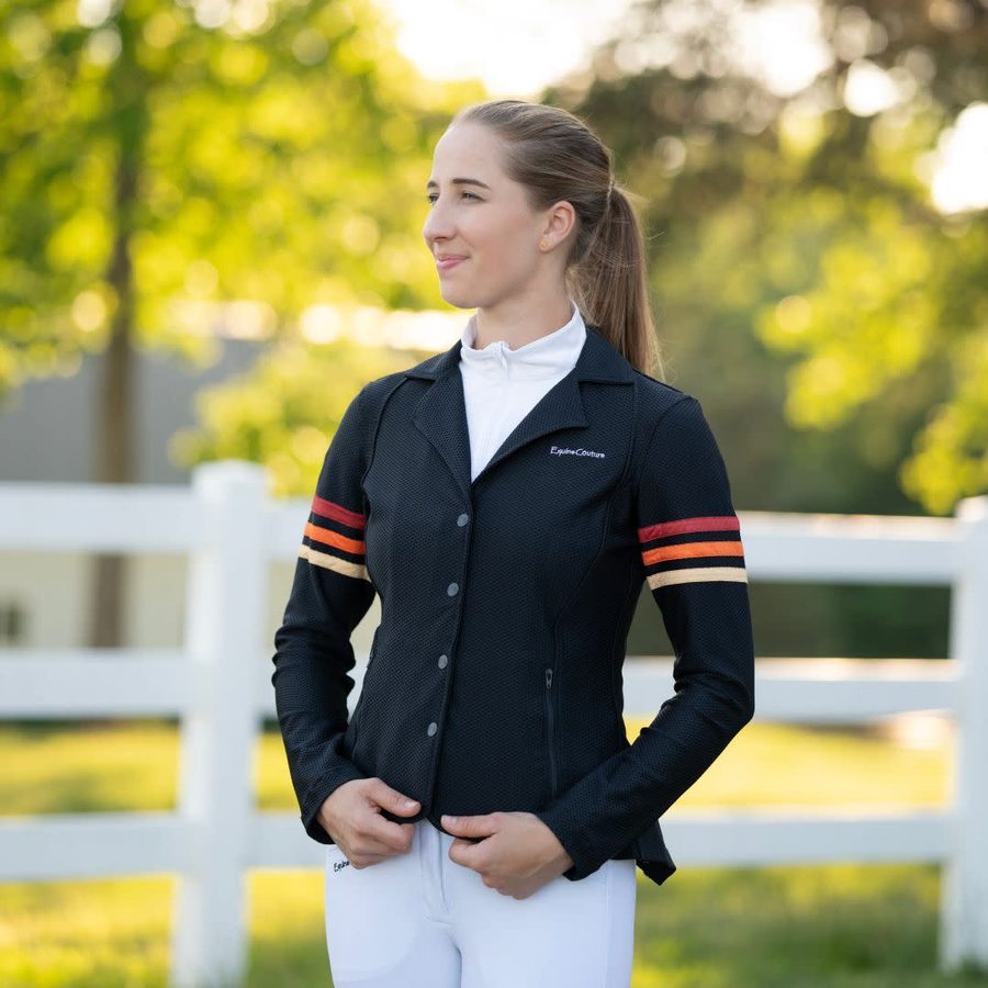 A young rider in a black Equine Couture EquiVent Gradient show coat with red arm stripes by a white fence