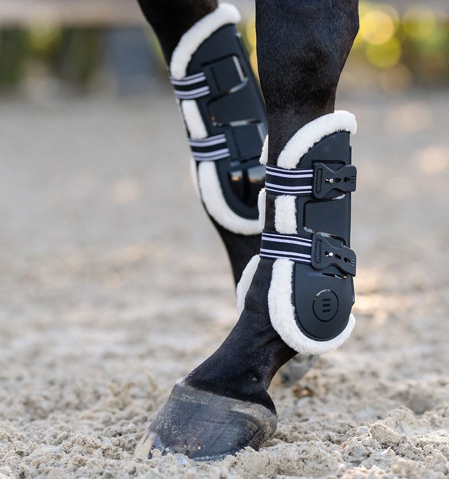 A dark bay horse in black EquiFit Essential Air2 front boots with fleece-lined edges on sand