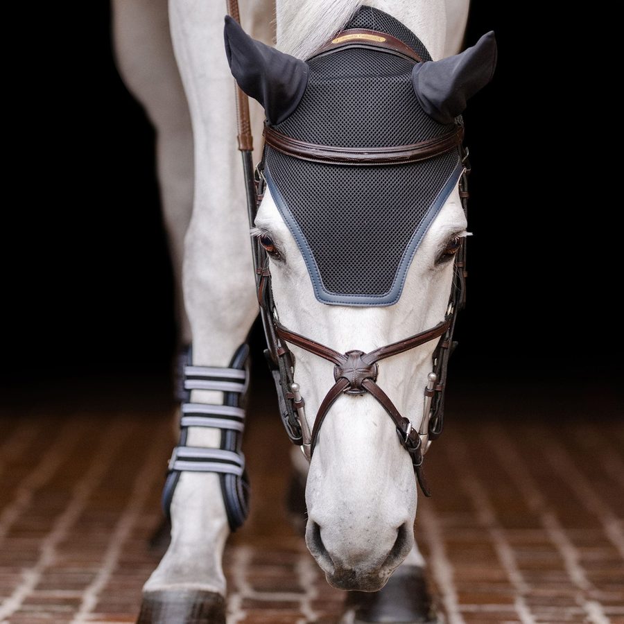 A grey horse in a navy EquiFit ear bonnet and black front boots
