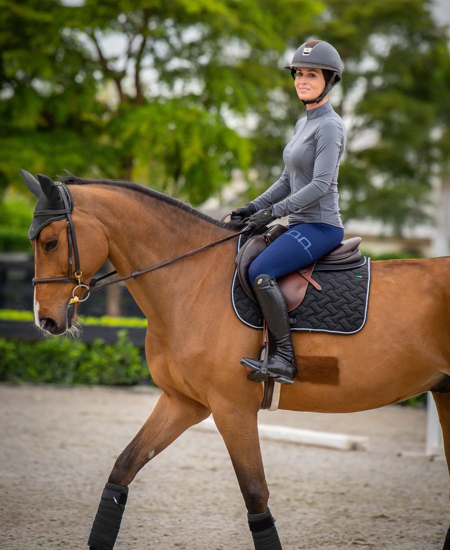 A rider in a gray Alessandro Albanese top and navy Platinum tights on a bay horse in an outdoor arena