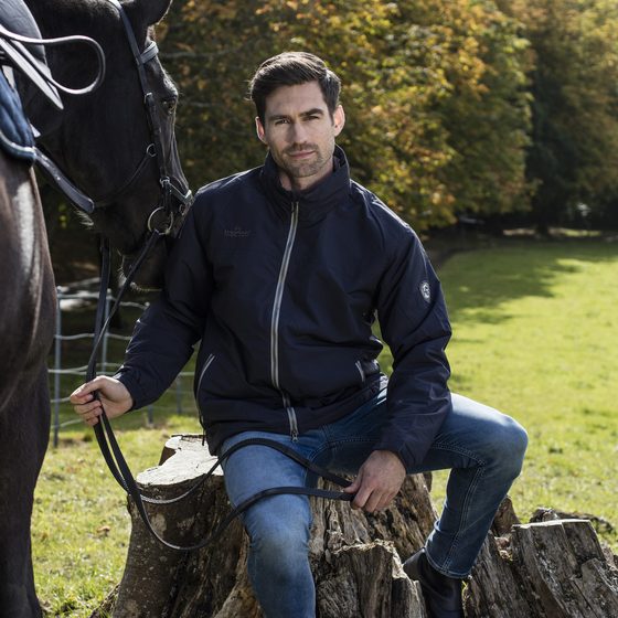 A man in a Horseware Corrib jacket sitting on a tree stump beside his horse