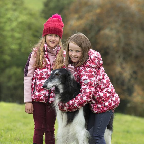 Two girls in Horseware quilted vests hugging a dog in a field