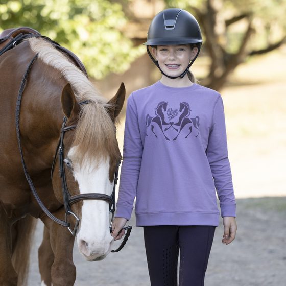 A smiling girl in a Kerrits horse sweatshirt and helmet leading her pony