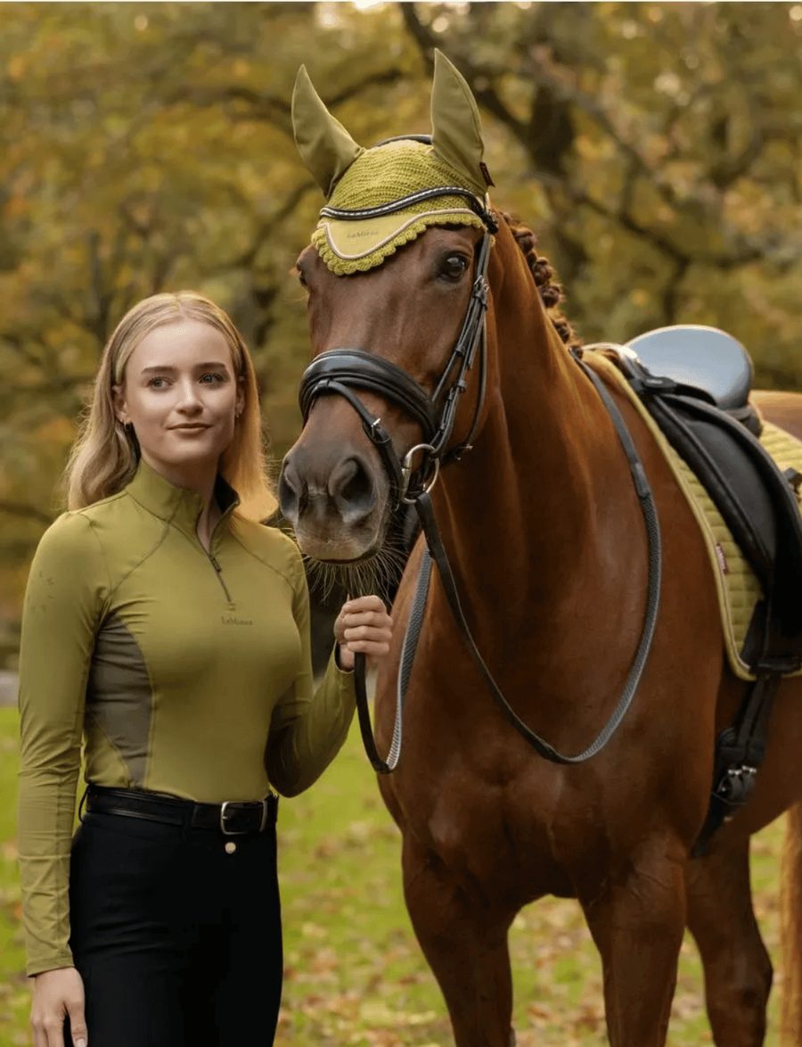A rider in an olive LeMieux base layer with her chestnut horse in a matching olive ear bonnet and saddle pad
