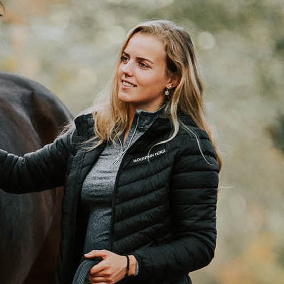 A smiling rider in a black Mountain Horse puffer jacket walking her horse