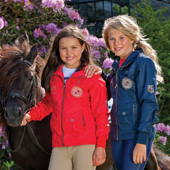 Two smiling girls in tall riding boots with their ponies