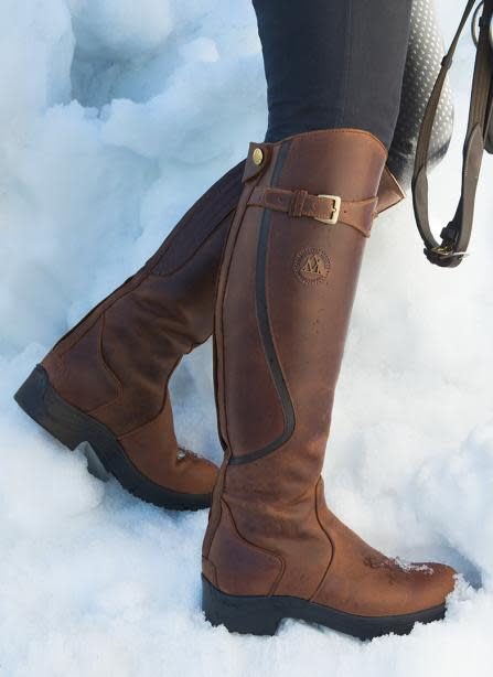 A rider in brown Mountain Horse Snowy River winter tall boots standing in deep snow