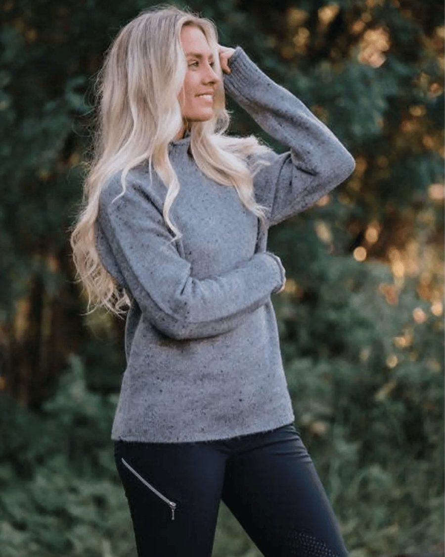 A smiling rider in a grey Mountain Horse crew sweater outdoors in autumn