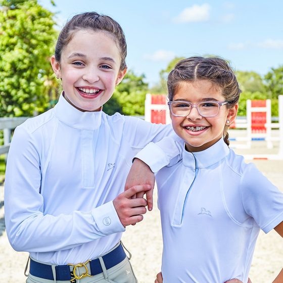 Two smiling girls in RJ Classics show shirts and breeches at a horse show