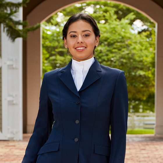A smiling rider in a navy RJ Classics Skylar show coat under a stone archway