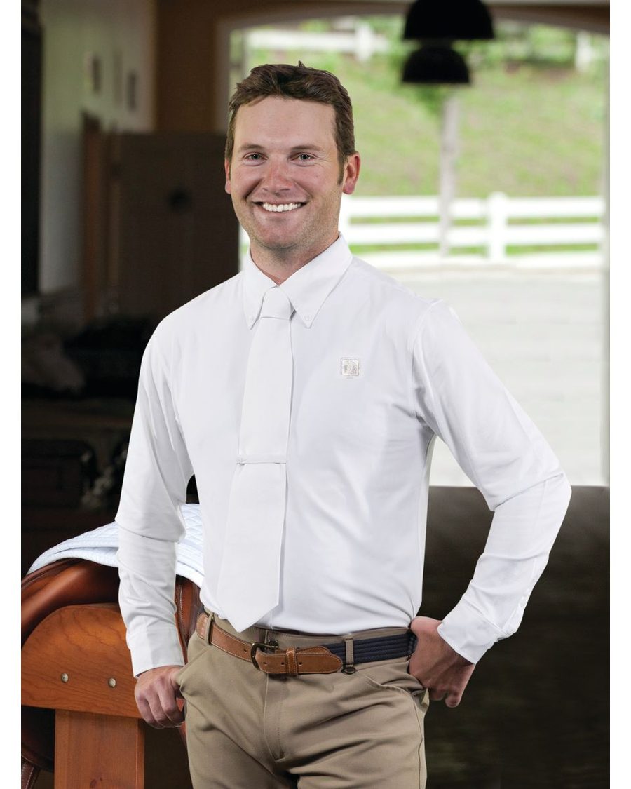 A smiling rider in a white Romfh show shirt and tan breeches in a barn aisle