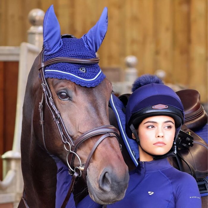 A bay horse in a navy ear bonnet beside a rider in a matching navy hat and top