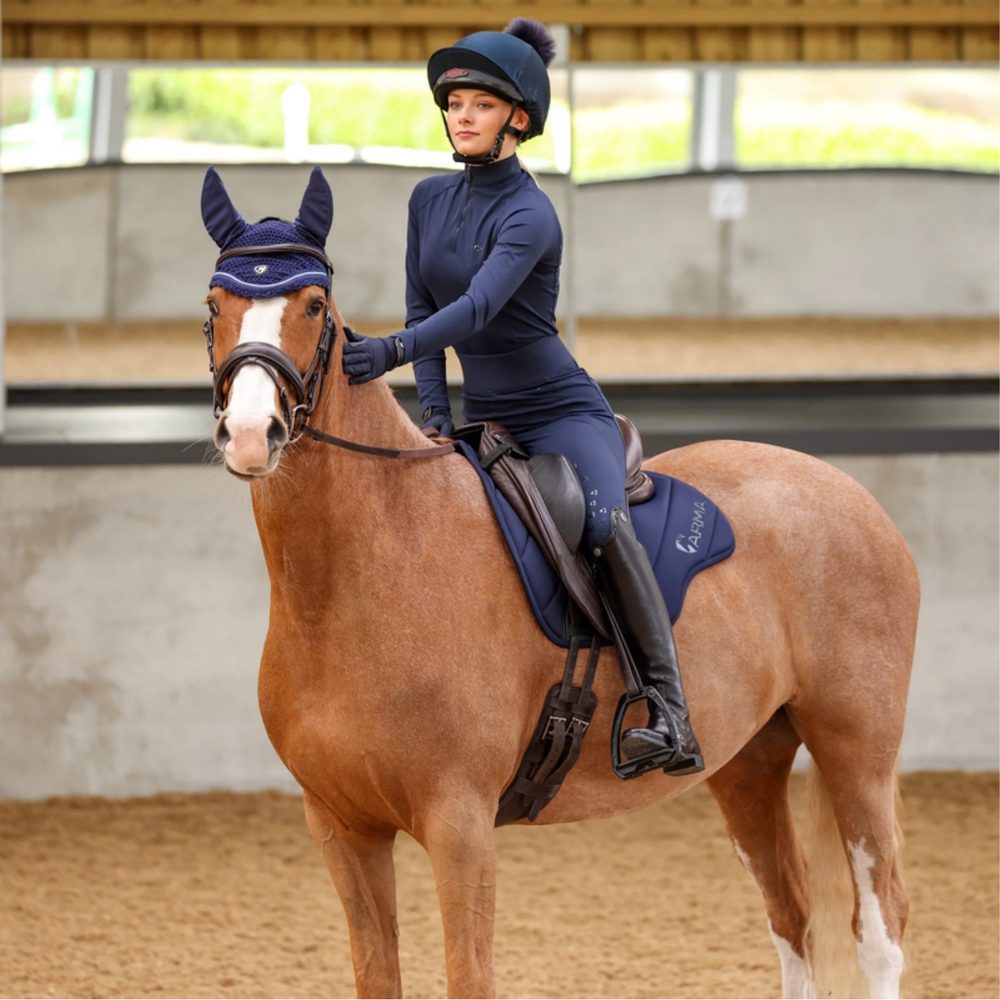 A rider in a navy Shires Aubrion top on a chestnut pony with a navy Shires ARMA saddle pad