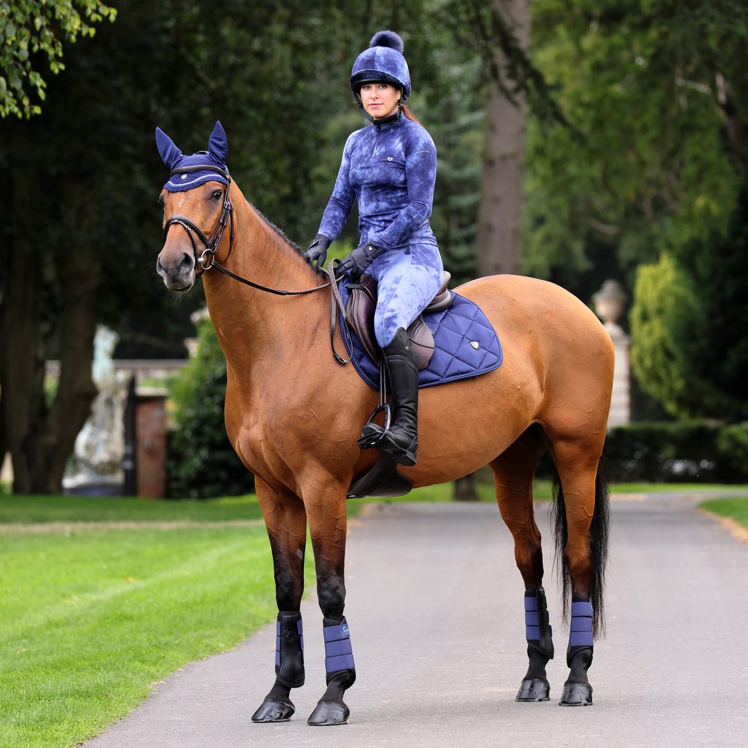 Rider in a navy tie-dye Shires Aubrion Revive base layer and riding tights on a bay horse
