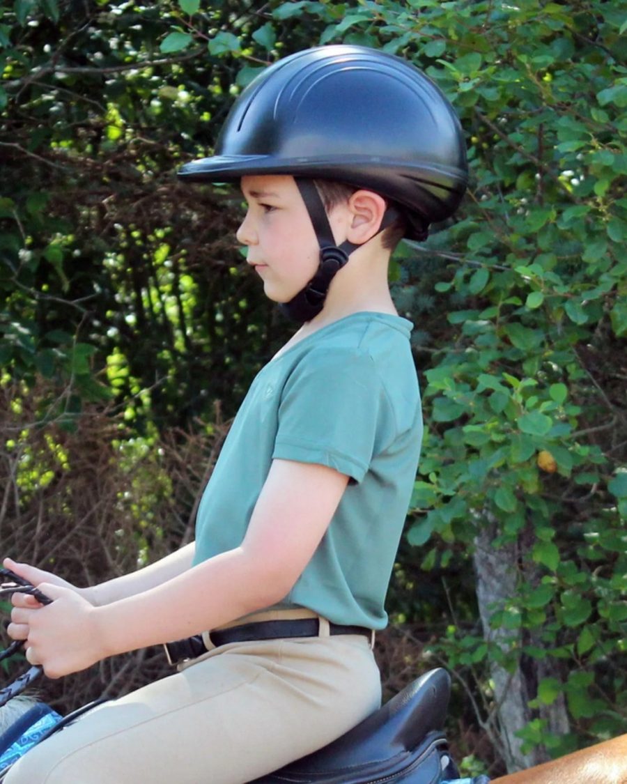 A young rider in a navy TuffRider helmet and teal shirt in the saddle