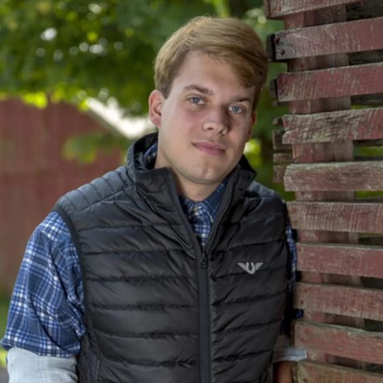 A young man in a black TuffRider puffer vest by a barn