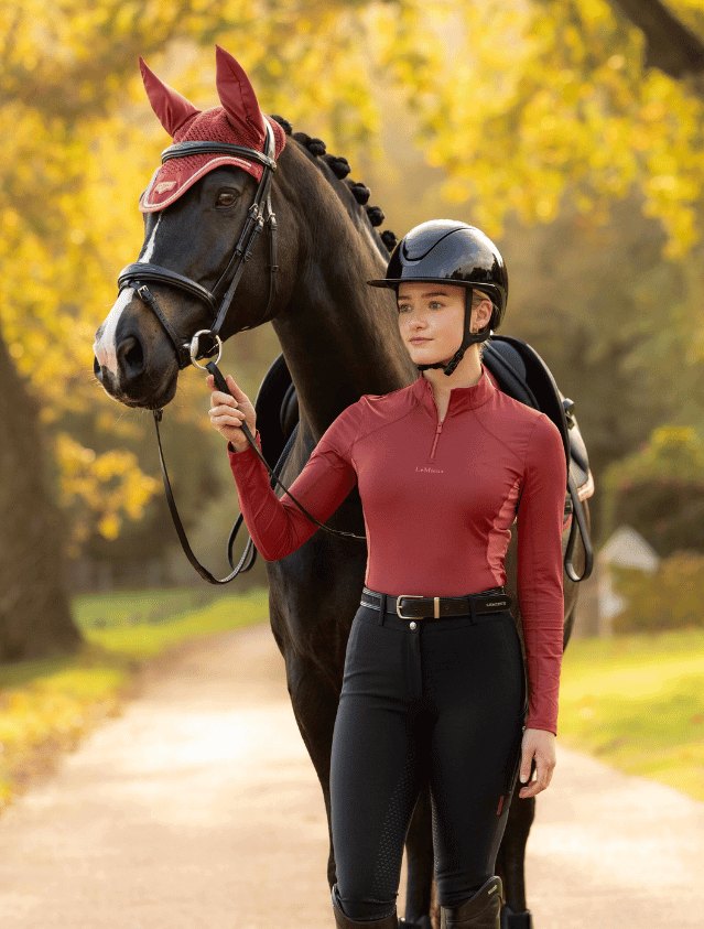 A rider in a burgundy top standing with her horse