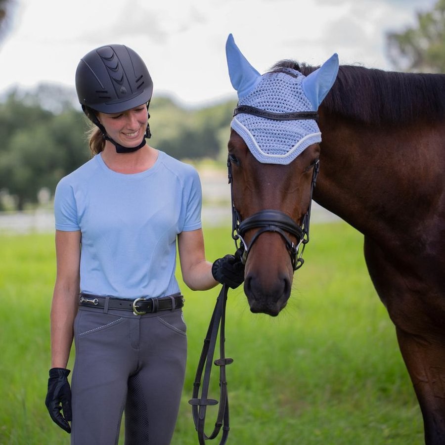 A rider in a helmet and gloves standing with her horse in a field