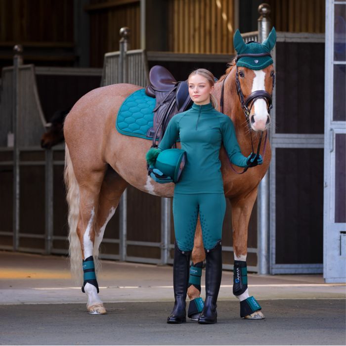 A chestnut horse and a rider in matching teal Shires ARMA and Shires Aubrion in a barn aisle