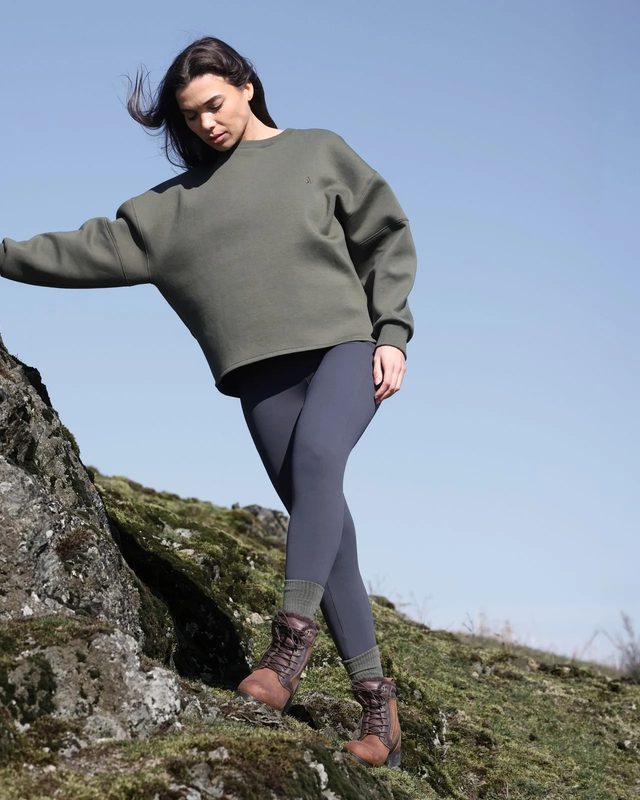 A rider in an olive Shires Aubrion sweatshirt and grey riding tights on a rocky hillside